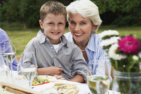 祖母坐在花园餐桌旁的快乐小男孩的画像