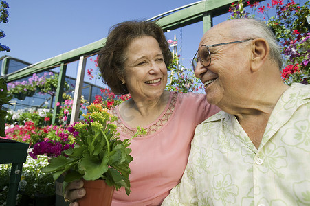 苗圃花丛中一对微笑的老年夫妇的特写