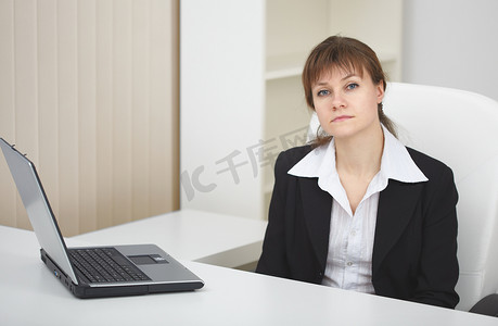 严肃的女人坐在带笔记本电脑的浅色办公室的桌子旁