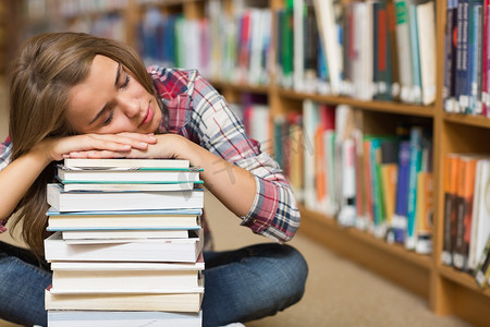 坐在图书馆地板上靠着一堆书睡觉的学生