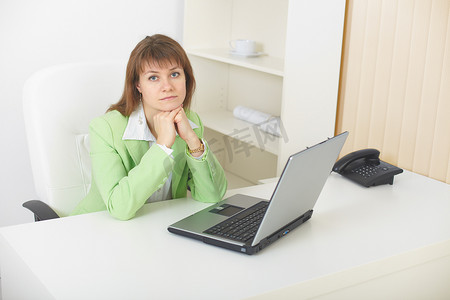 带笔记本电脑的年轻女性坐在浅色办公室的桌子旁