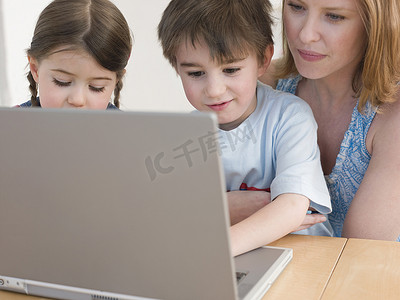 母亲和孩子在家里的餐桌上使用笔记本电脑