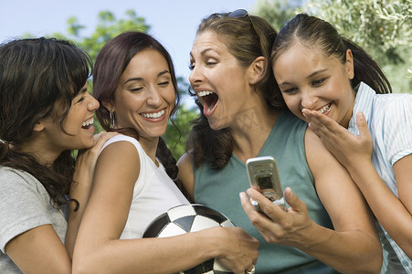 兴奋的四名年轻女性在户外微笑着看着手机