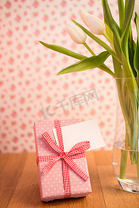 粉色圆点摄影照片_木桌上的郁金香花瓶，上面有粉色包装的礼物和空白卡片