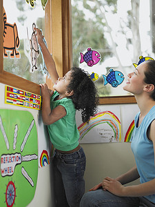 老师和女孩用剪纸装饰学校窗户的侧视图