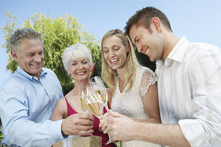父亲的肩摄影照片_快乐的年轻和年长夫妇在户外举着香槟杯