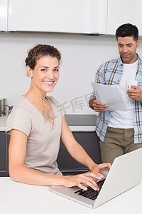 微笑的女人在伴侣看报纸时使用笔记本电脑
