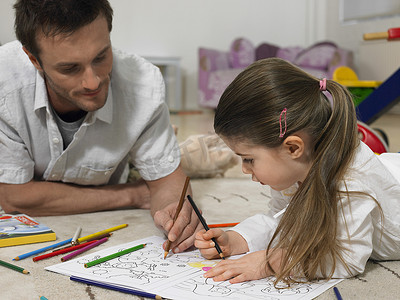 涂色画摄影照片_小女孩和父亲一起在家里的地板上涂色书