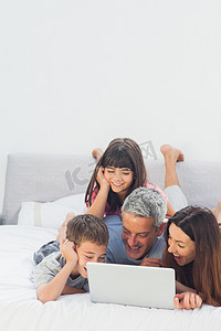 箭头向下动图摄影照片_幸福的家庭躺在床上使用他们的笔记本电脑