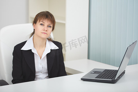 严肃的女人坐在带笔记本电脑的浅色办公室的桌子旁