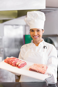 微笑的女厨师在厨房里拿着切肉托盘