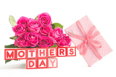 拼写母亲节的木块旁边的一束粉色玫瑰和粉色礼物