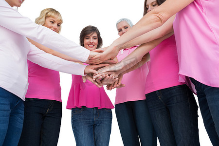 因患乳腺癌而身穿粉红色衣服的热心女性围成一圈，手牵着手看着相机