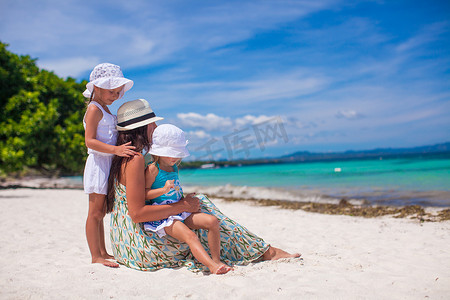 阳光明媚的日子里，时尚年轻母亲和她的两个孩子在异国情调的海滩上的后视