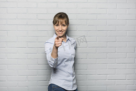 微笑的可爱女人用手指指着砖墙