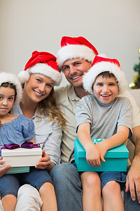 戴着圣诞帽的家人在沙发上拿着礼物