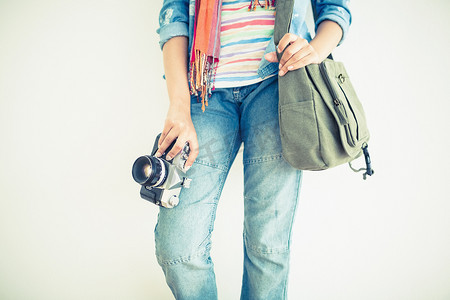 肩包摄影照片_拿着照相机和单肩包的牛仔裤的妇女