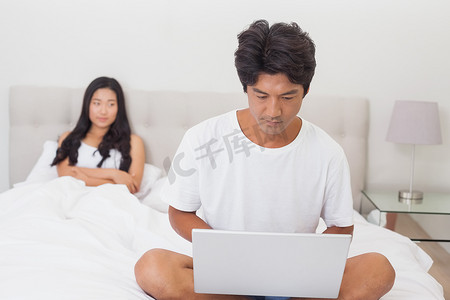 看着男朋友在床尾使用笔记本电脑的女人