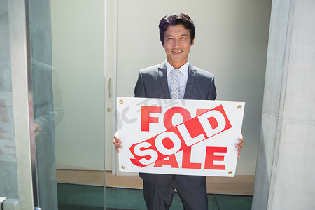 自信的房地产经纪人站在前门，展示已售出的标志