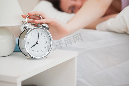 昏昏欲睡的女人躺在床上，把手伸向闹钟