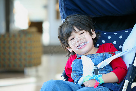 巡回演出的演员摄影照片_可爱的脑瘫残疾男孩在婴儿车里微笑
