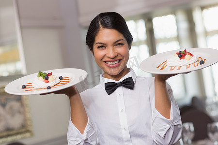 酒店女服务员摄影照片_拿着两个点心盘子的俏丽的女服务员