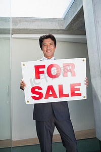 房子待售摄影照片_自信的房地产经纪人站在前门展示待售标志