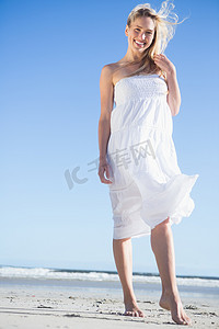 穿着白色连衣裙的金发女郎在沙滩上对着镜头微笑