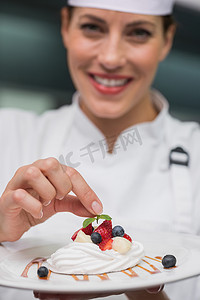 餐饮老板摄影照片_微笑的厨师将薄荷叶放在蛋白甜饼盘上