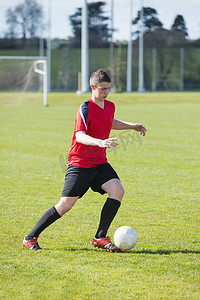 足球球场摄影照片_穿红色衣服的足球运动员在球场上踢球