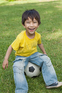 可爱的小男孩坐在公园的足球上