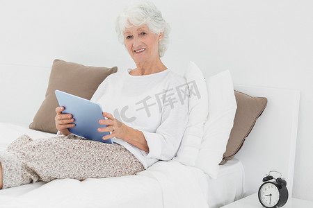 卧室桌子摄影照片_微笑的老妇人使用数字平板电脑