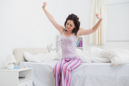 昏昏欲睡的女人在床上伸展双臂