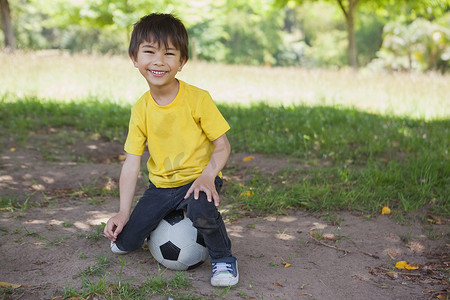 一个可爱的男孩在公园里坐在足球上的肖像