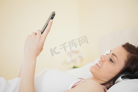 微笑的女孩躺在床上用智能手机听音乐