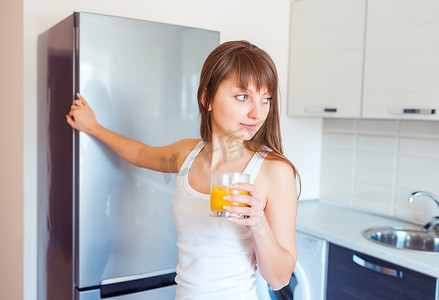 年轻的白人黑发女孩在厨房里喝着一杯果汁
