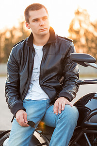 骑摩托的男人摄影照片_穿着皮夹克的骑自行车的人坐在他的摩托车上