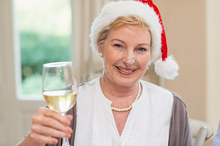 戴着圣诞帽的微笑成熟女人用白葡萄酒敬酒