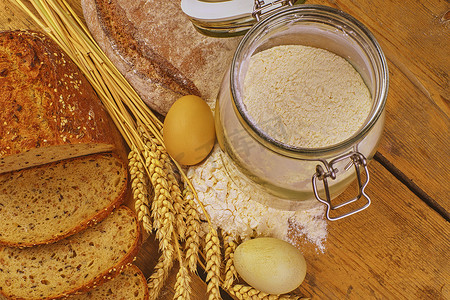 面包、面包片、小麦粉、鸡蛋和木头背景上的谷穗。
