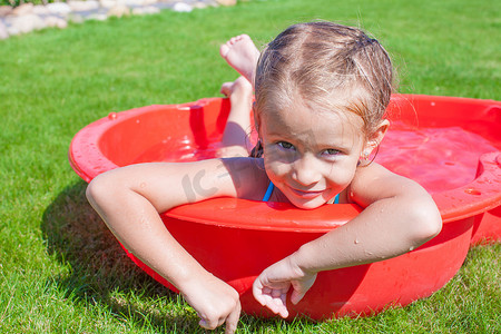 洗澡摄影照片_在小泳池享受假期的放松迷人小女孩的画像