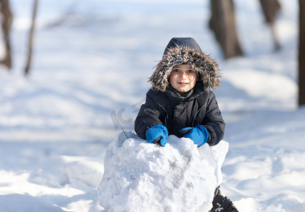 孩子玩雪摄影照片_在冬季公园玩雪的可爱男孩