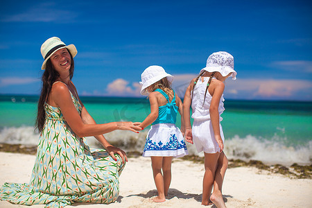 阳光明媚的日子里，年轻的母亲和她的两个时尚孩子在异国情调的海滩上