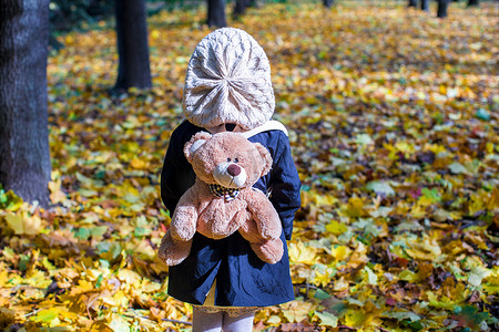 秋日阳光明媚的森林里背着背包熊的迷人小女孩的后视