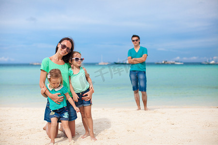 前景是妈妈和她可爱的女儿，背景是爸爸在海滩上