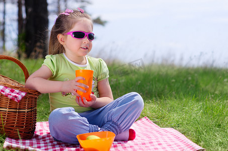 坐在草地摄影照片_带野餐篮和塑料杯的小女孩