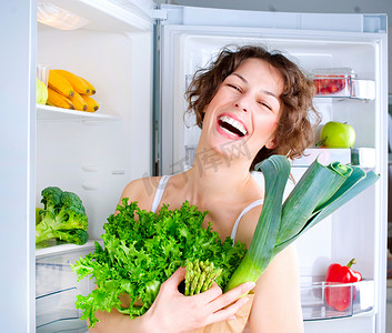 在冰箱附近的美丽的少妇用健康食物