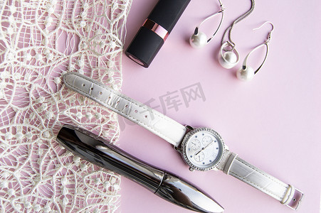 平躺式女装配饰拼贴有时尚手表、耳环和吊坠，配以白色珍珠、口红、睫毛膏，采用蕾丝粉红色背景