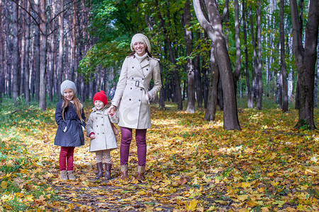 在温暖的阳光明媚的日子里，年轻的母亲和她可爱的女儿们在黄色的秋天森林里散步