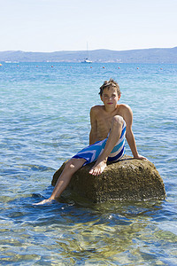 可爱的十一岁男孩坐在海中的岩石上