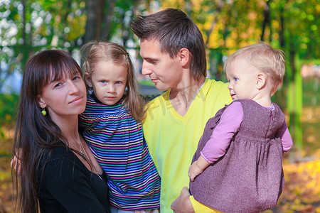 秋黄摄影照片_年轻迷人家庭与两个 kida 在黄秋公园享受天气的肖像